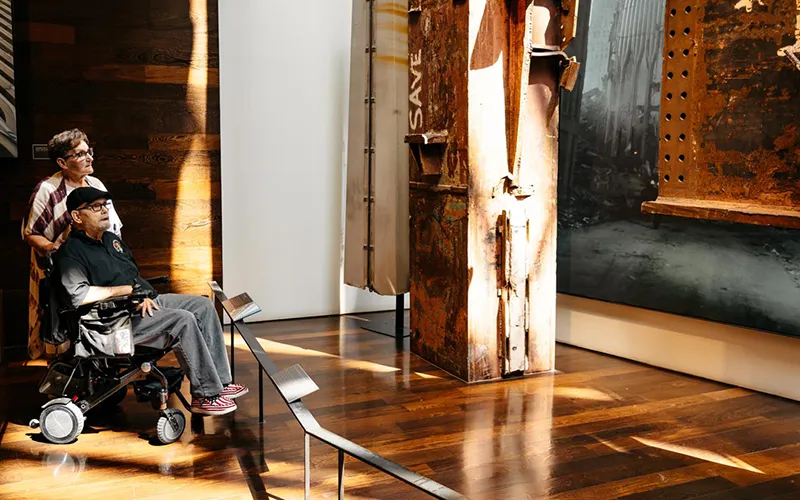 A man in a wheelchair and a woman look at an exhibit in the 9/11 museum