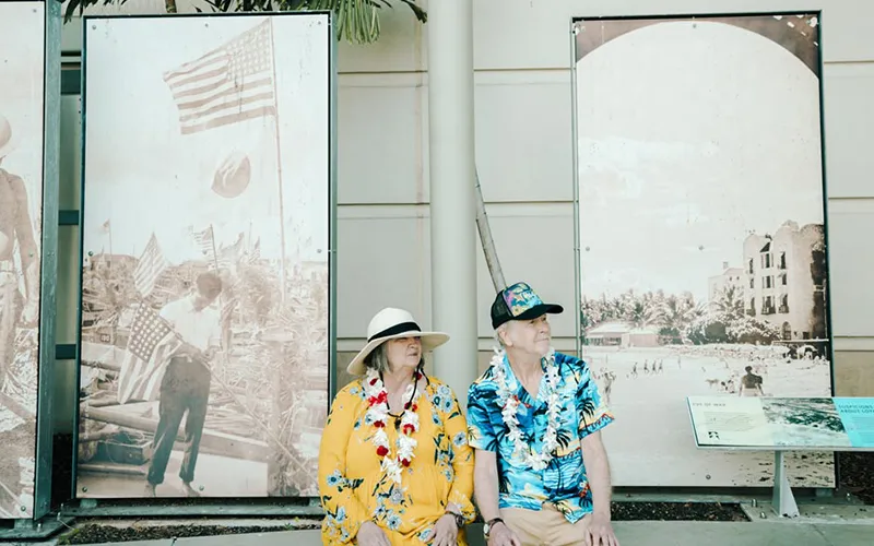 An older couple sits in front of a war memorial in Honolulu