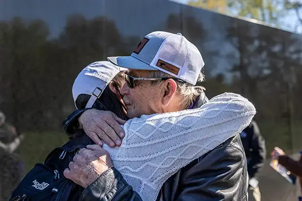 Two people embrace in front of the Vietnam Veterans Memorial Wall
