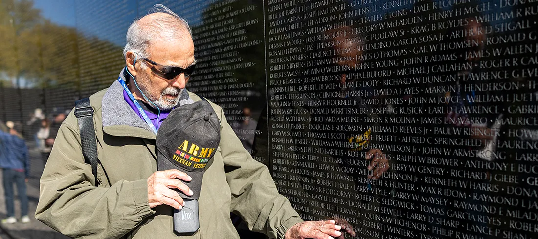 A man holding an Army hat touches the Vietnam Veterans Memorial Wall.