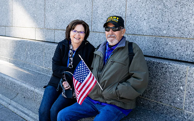 A man holds an American flag sitting next to a woman on a stone bench.