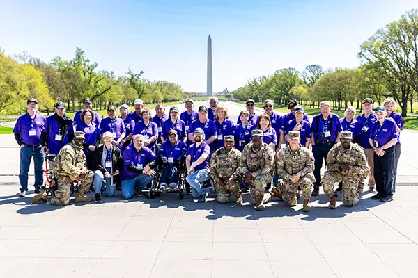 A tour group along with soldiers in uniform stand in front of the Washington Monument.