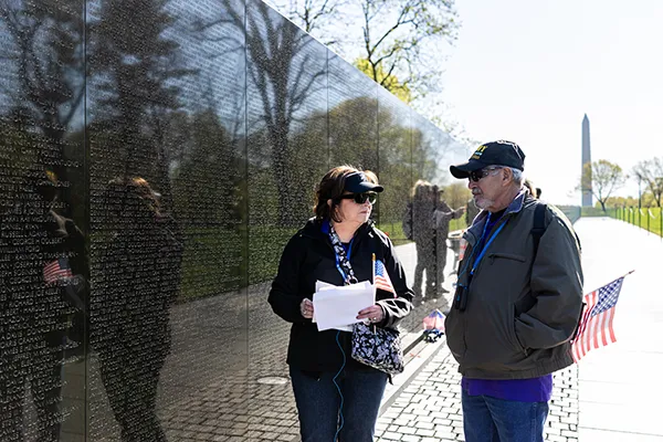 A man and woman look at one another next to the Vietnam Veterans Memorial Wall.