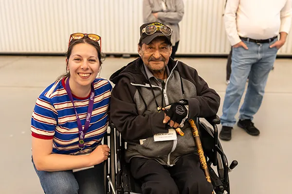 A woman kneels next to an older man in a wheelchair