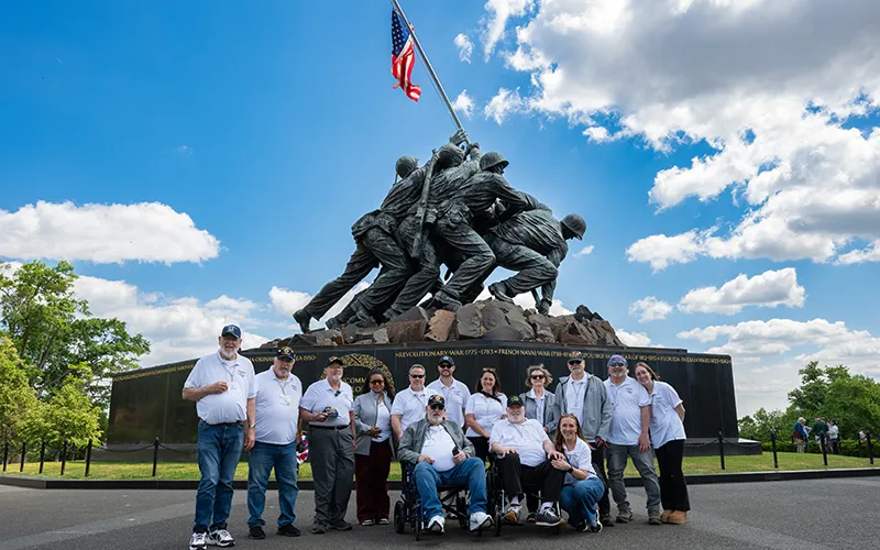 A group of older veterans stands in front of the US Marine Corps War Memorial in Washington, DC