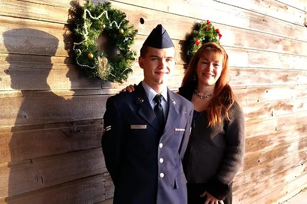 A woman stands next to a young man in a military uniform.
