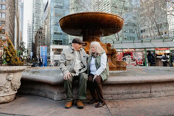 A man and woman sit beneath an outdoor fountain in the city.
