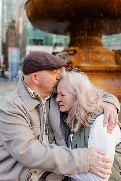 A man with a sad expression kisses a woman on her forehead.