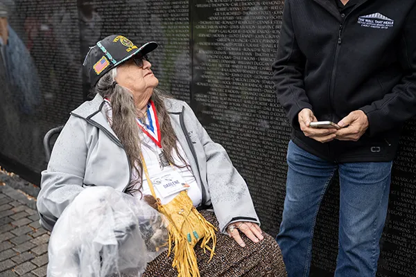 A woman Vietnam veteran sits in front of the Memorial Wall