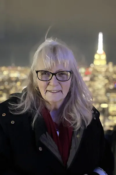 A woman smiles with New York City in the background, lit up at night.