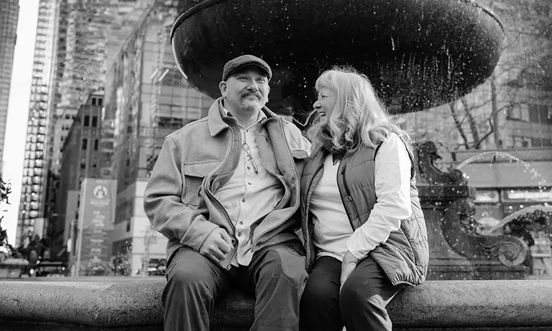 Two people laugh together while sitting outdoors underneath a fountain.
