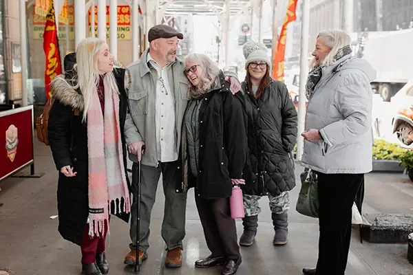 Four women greet a man on a city street.