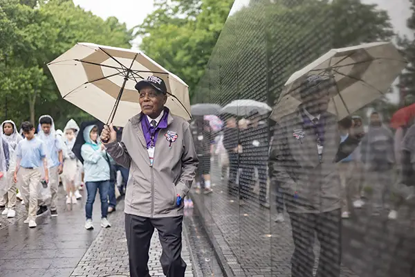 A man holds an umbrella while walking along the Vietnam Veterans Memorial Wall.