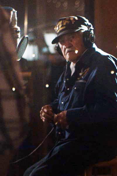 An older man sits in front of a studio microphone while wearing headphones