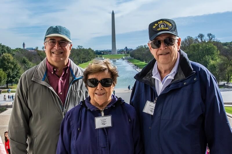 Two older men and a woman in front of the Washington Monument