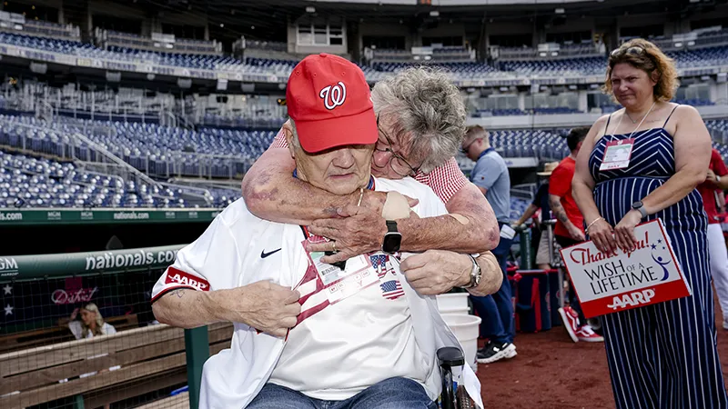 A woman hugs a man in a wheelchair at a baseball stadium.