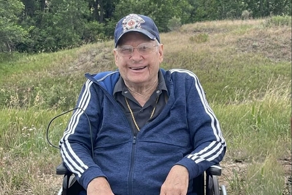 An older man sits in front of grassy rolling hills