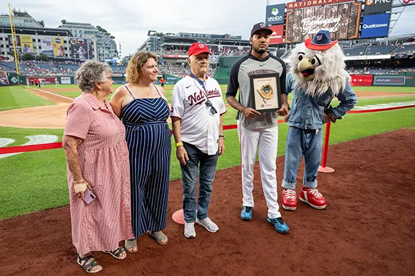 A family stands next to a baseball player and a mascot on a ball field.