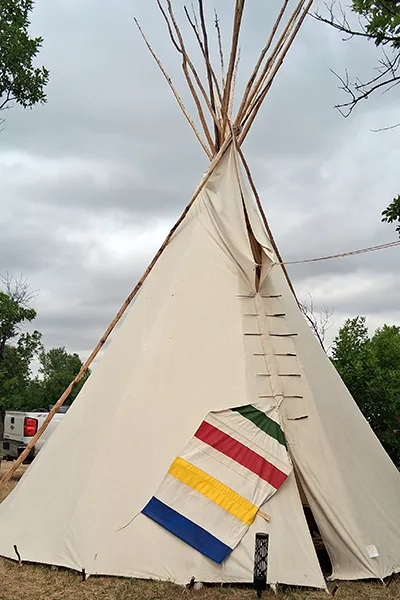 A Native person wearing traditional regalia rides a horse past a truck.