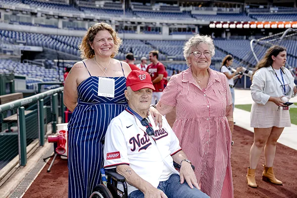 A man in a wheelchair sits with two women on a baseball field.