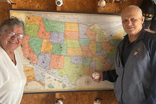 A man and woman stand on either side of a U.S. map with pins to mark locations.