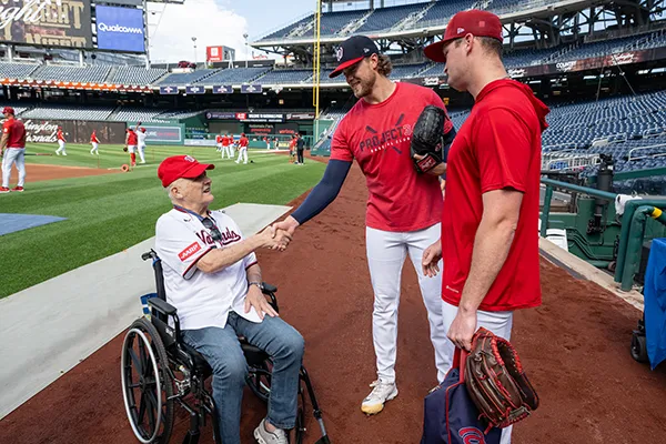 A man in a wheelchair shakes hands with a professional baseball player.