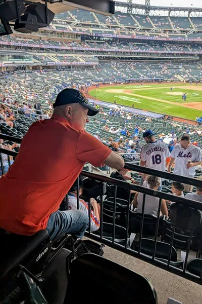 A man looks over a balcony railing inside a baseball stadium.