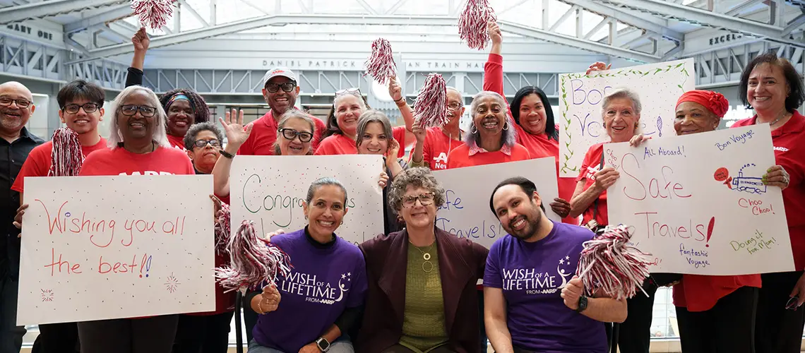 A woman is surrounded by Wish of a Lifetime and AARP volunteers holding signs for safe travels.